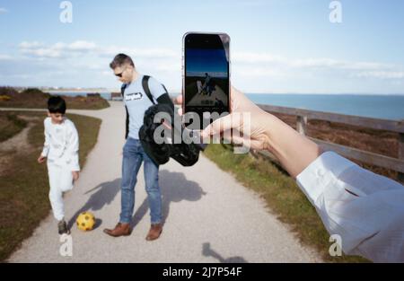 Frau, die mit ihrem Telefon Fotos von ihrer Familie beim Fußballspielen machte Stockfoto