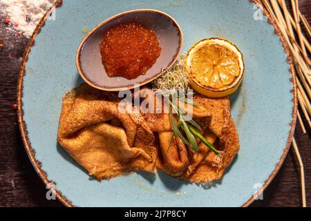 Pfannkuchen mit rotem Kaviar, Zitrone auf dem Tisch, Ei in Mehl, whea Stockfoto