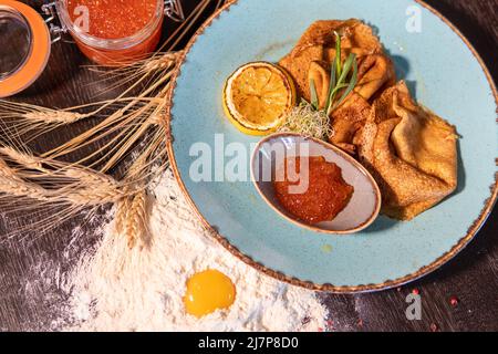 Pfannkuchen mit rotem Kaviar, Zitrone auf dem Tisch, Ei in Mehl, whea Stockfoto