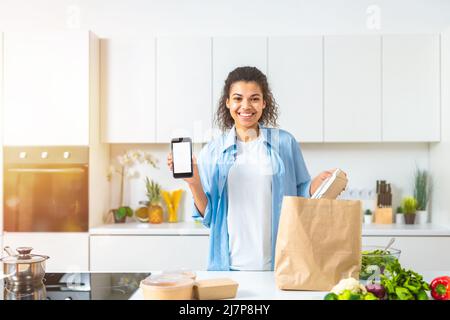 Lächelnde Frau mit einer Einkaufstasche, die online über das Smartphone bestellt und direkt zu Hause geliefert wurde Stockfoto