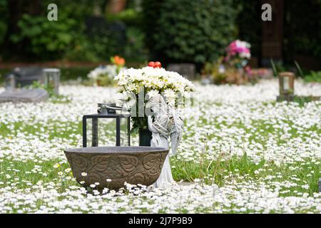 Kleines Urnengrab mit Engel auf einer mit Gänseblümchen bedeckten Frühlingswiese Stockfoto