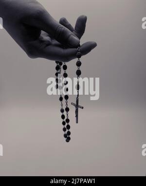 Die Hand einer Frau, die den Rosenkranz in schwarz-weißen Filtern hält. Stockfoto