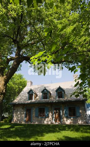 Altes 1740 Canadian fiieldstone Haus mit blauen Zierleisten und Zedernholz Schindeln Dach im Sommer. Stockfoto