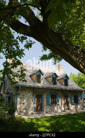 Altes 1740 Canadian fiieldstone Haus mit blauen Zierleisten und Zedernholz Schindeln Dach im Sommer. Stockfoto