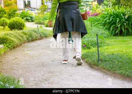 Eine Frau, die allein auf einem gewundenen Feldweg in einem Stadtpark inmitten üppiger grüner Vegetation spazieren geht. Botanischer Garten im Frühling, Sommertag. Eine Frau ist f Stockfoto