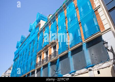 Rekonstruktion der Fassade eines historischen klassischen Wohnhauses an einer Stadtstraße an sonnigen Tagen gegen den Himmel. Blaue Fassade Konstruktionsgewebe bedeckt ein Stockfoto