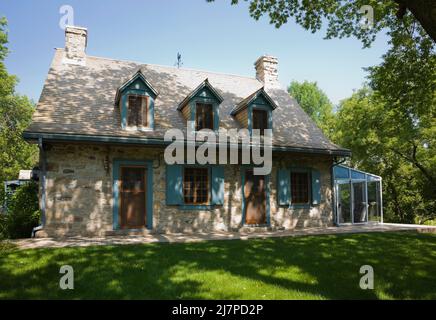 Altes 1740 Canadian fiieldstone Haus mit blauen Zierleisten und Zedernholz Schindeln Dach im Sommer. Stockfoto