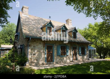 Altes 1740 Canadian fiieldstone Haus mit blauen Zierleisten und Zedernholz Schindeln Dach im Sommer. Stockfoto