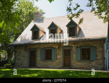 Altes 1740 Canadian fiieldstone Haus mit blauen Zierleisten und Zedernholz Schindeln Dach im Sommer. Stockfoto