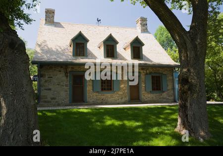 Altes 1740 Canadian fiieldstone Haus mit blauen Zierleisten und Zedernholz Schindeln Dach im Sommer. Stockfoto