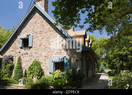 Altes 1740 Canadian fiieldstone Haus mit blauen Zierleisten und Zedernholz Schindeln Dach im Sommer. Stockfoto