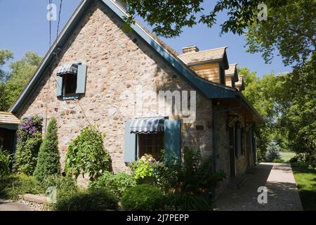 Altes 1740 Canadian fiieldstone Haus mit blauen Zierleisten und Zedernholz Schindeln Dach im Sommer. Stockfoto