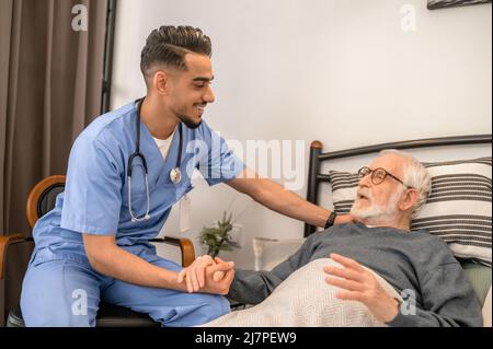 Lächelnder, freundlicher Arzt, der einen bettlägerigen Patienten besucht Stockfoto