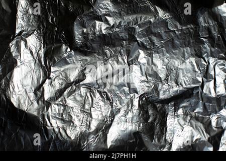 Folienstruktur. Zerknittert gerippte Folie. Unebene Hintergrundoberfläche reflektiert Licht. Stockfoto