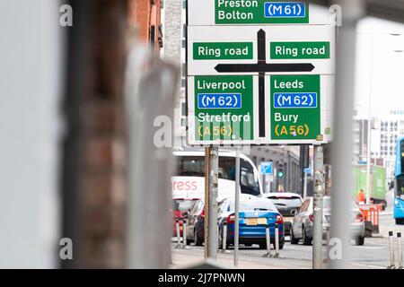 Straßenschild in der Innenstadt, das die Routen nach Liverpool anzeigt. Leeds, Stretford, Bury usw.; inmitten von viel Verkehr und urbaner Szene Stockfoto