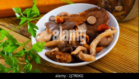Verschiedene eingelegte Pilze mit Petersilie und Zwiebeln in Scheiben Stockfoto