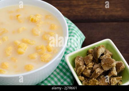 Traditionelles kolumbianisches Essen namens Mazamorra, basierend auf gekochtem, in Milch gelöstem Mais, begleitet von Panela in Stücken (süß aus Zuckerrohr). Dunkles Holz. Stockfoto