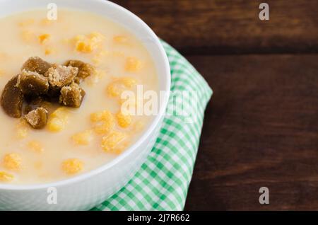 Traditionelles kolumbianisches Essen namens Mazamorra, basierend auf gekochtem, in Milch gelöstem Mais, begleitet von Panela in Stücken (süß aus Zuckerrohr). Dunkles Holz. Stockfoto