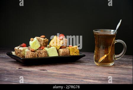 Eine Auswahl an türkischen Süßigkeiten auf einem Teller und eine Tasse heißen schwarzen Tee auf einem Holztisch. Nahaufnahme. Stockfoto