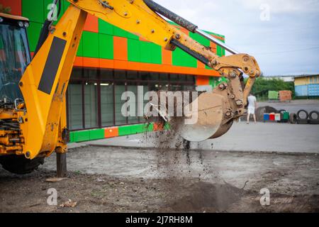 Bagger gräbt Boden. Konstruktionsdetails. Schwere Maschinen auf der Straße. Parkplatz wird erstellt. Reinigung des Ortes. Stockfoto