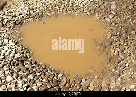 Pfütze auf der Straße. Pit auf Landstraße. Steine und Wasser. Schmutziges Wasser hatte sich in der Grube angesammelt. Stockfoto