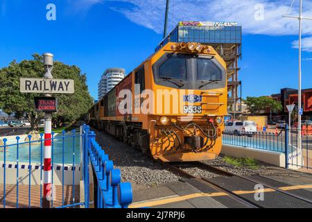 Eine Diesel-elektrische Lokomotive der KiwiRail DL-Klasse, die durch einen Bahnübergang in der Stadt Tauranga, Neuseeland, fährt Stockfoto