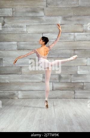 Ganzkörper-Rückansicht einer flexiblen Tänzerin, die mit erhobenem Bein eine Attitude Pose macht, während sie im Lichtstudio tanzt Stockfoto