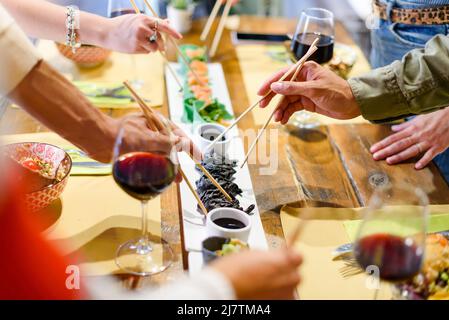 Anonyme Freunde aus einem hohen Blickwinkel treffen sich am Tisch mit asiatischen Gerichten und Gläsern Rotwein, während sie gemeinsam das Abendessen genießen Stockfoto