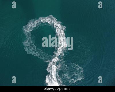 Luftaufnahme von oben nach unten von Wasserschaumspuren mit schönem tiefblauen Schatten des Ozeans. Schöne weiße Spur auf der ruhigen Meeresoberfläche hinter einem kleinen mächtigen Stockfoto