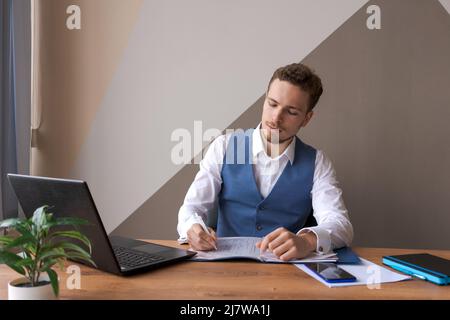 Geschäftsmann arbeitet in einem Büro mit Laptop und Dokumenten auf seinem Schreibtisch in Hemd und Weste mit Bart, ein Anwalt Berater. Das Konzept der erfolgreichen Menschen. Stockfoto