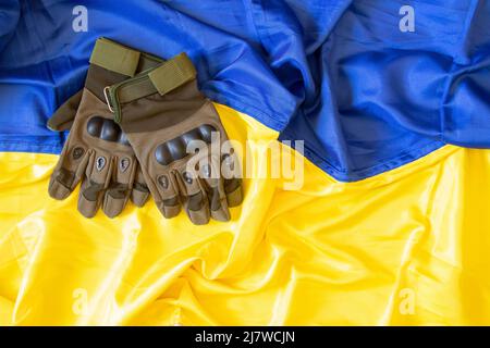 Militärische Schutzhandschuhe liegen auf der Flagge der Ukraine gelb-blau, der Krieg in der Ukraine, die Uniform eines Soldaten, die Armee der Ukraine Stockfoto