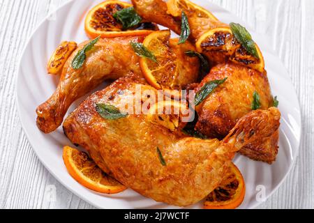 Nahaufnahme des gegrillten Hähnchengrillen von Orange auf weißem Teller mit Salbeiblättern, horizontale Ansicht von oben Stockfoto