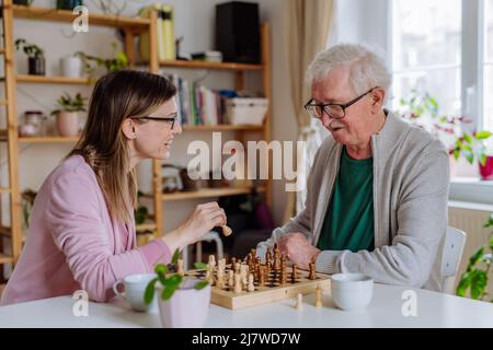 Erwachsene Tochter besucht ihren älteren Vater zu Hause und spielt gemeinsam Schach. Stockfoto