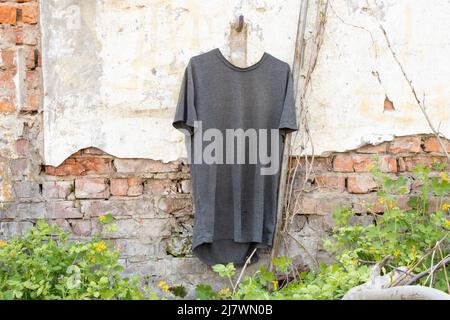 Graues T-Shirt an Kleiderbügeln, die in der Sonne, Mode und Trends an der Wand auf der Straße hängen Stockfoto