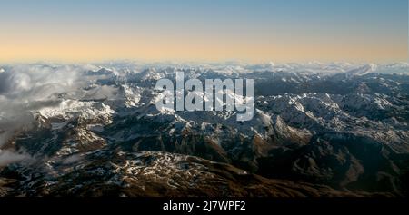 Fliegen über die Alpen - Blick auf den Flugzeugflügel über schneebedeckten Bergen. Schöne Luftlandschaftsansicht der Berge. Luftaufnahme von schneebedeckter M Stockfoto