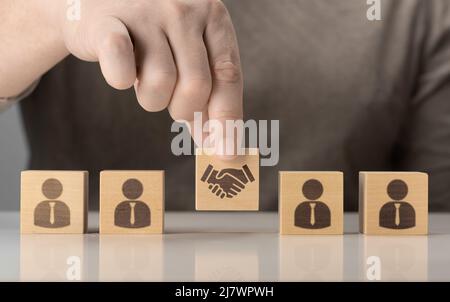 Geschäftsvertrag. Handschüttelns auf einem Holzwürfelblock vor einer menschlichen Ikone für Geschäftsabschlusses und Vertragskonzept. Geschäftliche Kommunikation Stockfoto