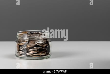 Münzen im Glas. Währungsgeld auf dunkelgrauem Hintergrund für Geschäfts- und Finanzkonzept. Kopierraum. Glas voller Münzen. Business, Finanzen, Sparen Stockfoto