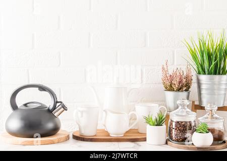 Das Innere der Küchenarbeitspütte mit Wasserkocher, Tassen, Kaffeekocher und verschiedenen schönen Zimmerpflanzen in modernen Töpfen Stockfoto