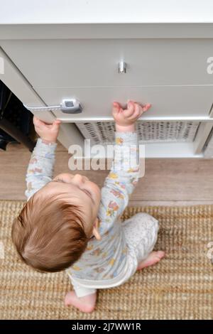 Kleinkind Baby Junge reißt aus einem Schrank Schublade mit seiner Hand. Das Kind hält den Schranktürgriff, kleines Kind Stockfoto