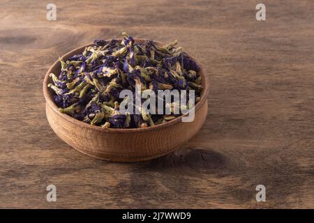 Blauer Tee Anchan Thai Farmer Butterfly Pea Tee. Bio getrocknete Blütenknospen und Blütenblätter in einer Holzschale auf dem Hintergrund. Krautige Rebe Clitoria ternatea. Stockfoto