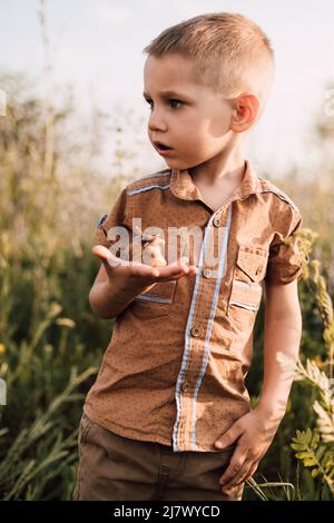 Ein kleiner Junge steht in der Natur im Gras und hält eine Schnecke in der Hand Stockfoto