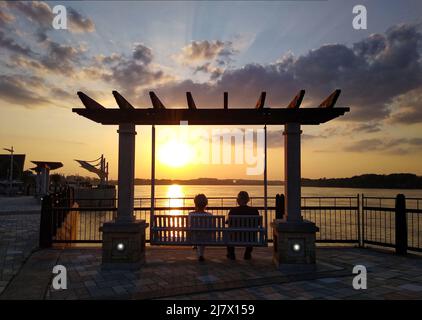 Ein unidentifiziertes Paar beobachtet den Sonnenuntergang, während es am Dienstag, den 10. Mai 2022, auf einer Schaukel im Smothers Park am Ohio River in Owensboro, Daiess County, KY, USA. Smothers Park war Owensboros erster Stadtpark, der 1816 als Riverfront Park gegründet und 1963 zu Ehren des ersten Siedlers der Stadt, William 'Bill' Smeathers (auch bekannt als Bill Smithers und Bill Smothers), in Smothers Park umbenannt wurde. (APEX MediaWire Foto von Billy Suratt) Stockfoto