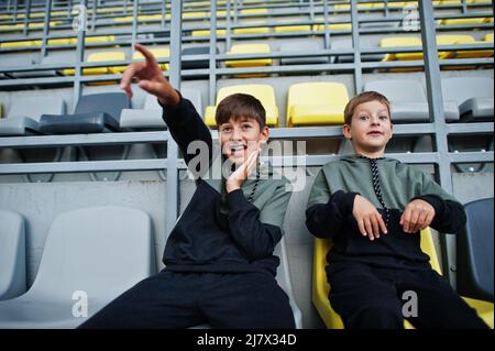 Zwei Brüder unterstützen ihre Lieblingsmannschaft und sitzen auf dem Sportpodium im Stadion. Stockfoto