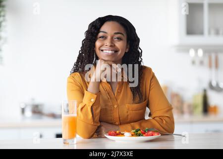 Glückliche junge schwarze Frau, die richtiges Frühstück, Kücheneinrichtung hat Stockfoto