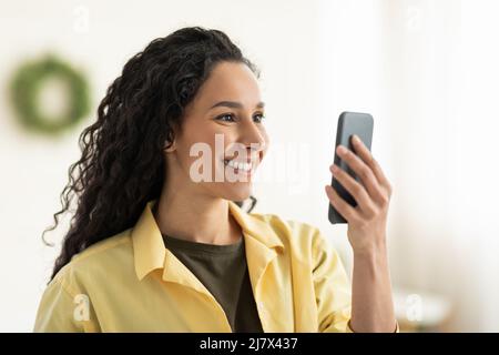 Lächelnde junge Frau mit Smartphone zu Hause, Nahaufnahme Stockfoto