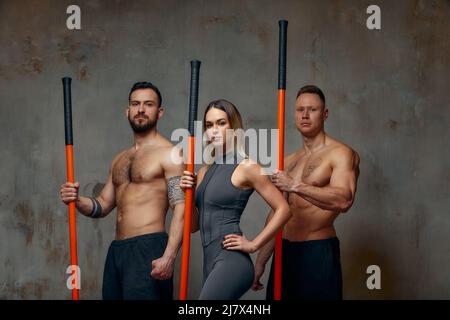 Menschen stehen zusammen und üben Stöcke. Karate-Meister posieren mit Stöcken im Studio zusammen. Stockfoto