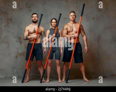 Menschen stehen zusammen und üben Stöcke. Karate-Meister posieren mit Stöcken im Studio zusammen. Stockfoto