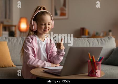 Wenig Schulmädchen Mit Laptop Gesturing Daumen Nach Oben Sitzen Zu Hause Stockfoto