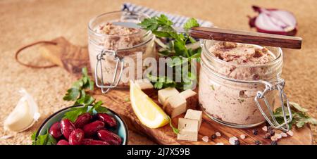 Von oben köstliche vegetarische Leberwurst in Pint-Gläsern mit Zitronenscheiben und frischer Petersilie auf Holzbrett in der Nähe einer Schüssel marinierte rote Bohnen serviert Stockfoto