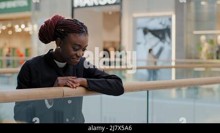 Schöne afroamerikanische Mädchen Frau mit stilvollen Frisur in schwarzem Mantel steht drinnen halten Geländer Blick in die Ferne genießen Wochenende Stockfoto